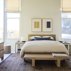 a large bed in a bedroom next to two windows with pictures on the wall above it