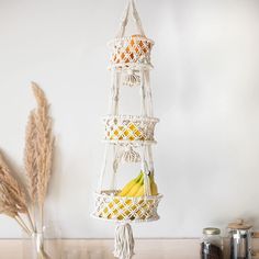 three tiered hanging fruit basket with bananas and straws in front of a white wall