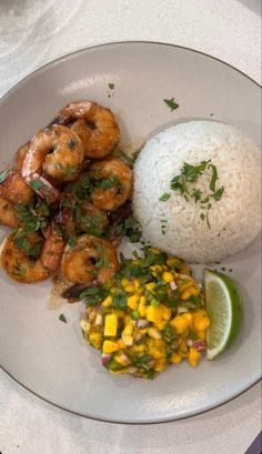 a white plate topped with rice and shrimp next to a slice of lime wedges