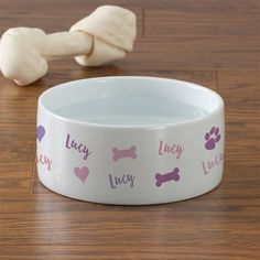 a white dog bowl with pink and purple paw prints on it next to a bone