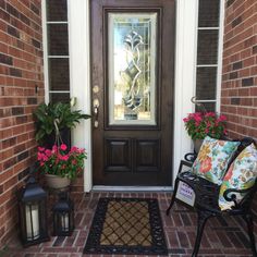 the front door is decorated with flowers and plants, along with a welcome mat on the brick walkway