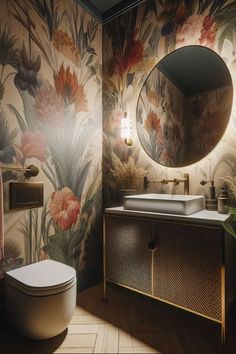 a bathroom with floral wallpaper and a round mirror above the sink, along with a toilet