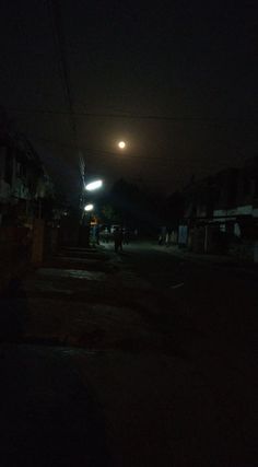 a dark street at night with the moon in the distance