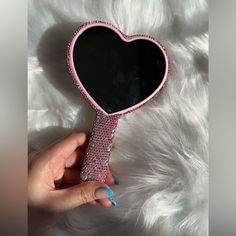 a hand holding a pink heart shaped mirror on top of a white fur covered surface