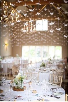 a room filled with lots of tables covered in white linens and paper cranes hanging from the ceiling