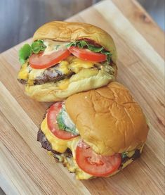 two hamburgers sitting on top of a wooden cutting board next to eachother