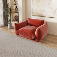 a red chair sitting on top of a wooden floor in front of a large painting