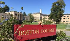 a red sign that says boston college in front of a building with trees and bushes