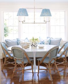 a dining room table with blue chairs and pillows on it in front of a window