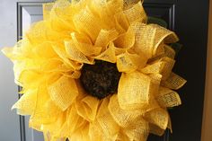 a large yellow sunflower is hanging on the front door with burlap mesh