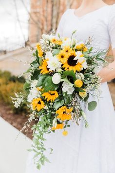 a bride holding a bouquet of sunflowers and greenery