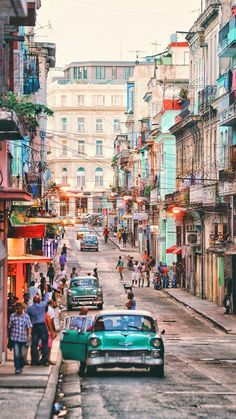 an old car is parked on the street in front of some buildings and people walking around