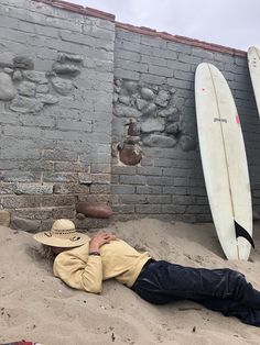 a man laying in the sand next to two surfboards and a brick wall with graffiti on it