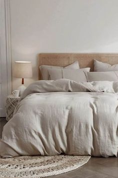 a bed with white linens and pillows in a neutral bedroom, next to a wicker headboard