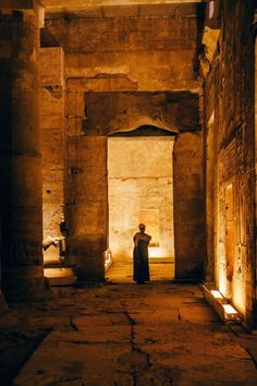 a man standing in an ancient building with columns and light coming through the doorways