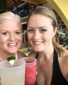 two women pose with drinks in front of them