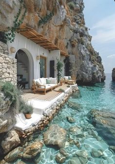 a house sitting on top of a rocky cliff next to the ocean with water in front of it