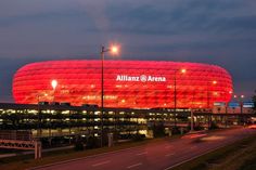 an allianz arena lit up at night with cars passing by on the road