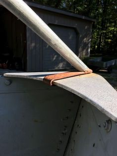 the back end of an old boat in front of a building with a shed and trees behind it