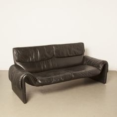 a black leather couch sitting on top of a cement floor next to a white wall