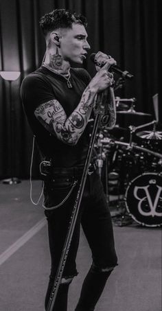 a man standing in front of a microphone next to another person with tattoos on their arms