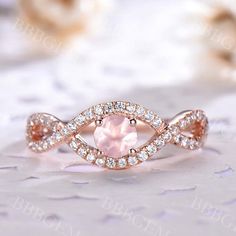 a pink diamond ring on top of a white table with some flowers in the background