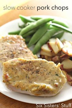 a white plate topped with pork chops next to green beans and potatoes on a wooden table