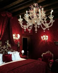 a bedroom with red walls and chandelier hanging from the ceiling, while a woman stands in the doorway