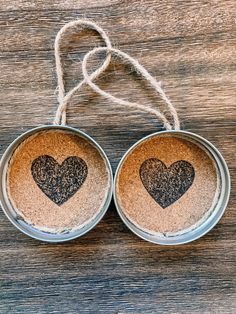 two tin canisters with hearts on them hanging from twine rope against a wooden table