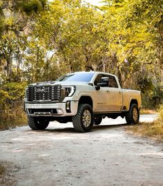 a white truck is parked on the side of a dirt road in front of trees