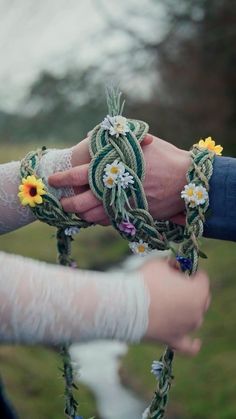 two people are holding hands with flowers on the string attached to their wristbands