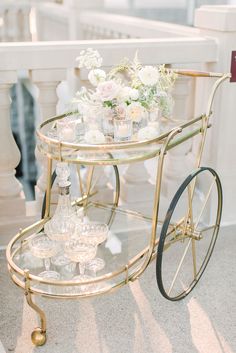 a gold bar cart filled with glasses and flowers