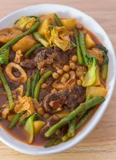 a white bowl filled with meat and veggies on top of a wooden table