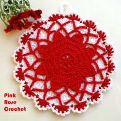 a crocheted doily with red and white flowers on the side next to it