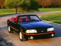 a black convertible car parked on the side of a road in front of a tree