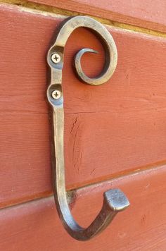 an iron hook on the side of a red door with a metal handle hanging from it