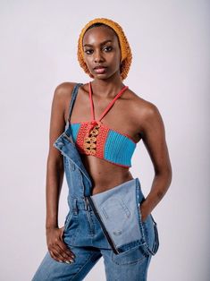 a woman in overalls and a crocheted hat poses for a photo with her hands on her hips