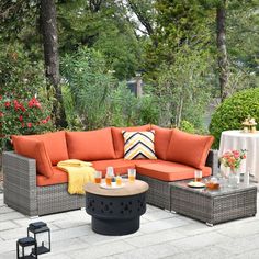 an outdoor seating area with orange cushions and coffee table, surrounded by flowers and greenery