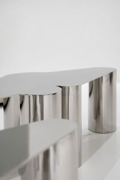 two silver tables sitting on top of a white floor next to each other in front of a white wall