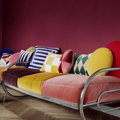 a couch with many pillows on it in front of a purple wall and wooden floor