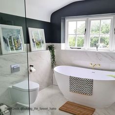 a white bath tub sitting next to a toilet in a bathroom under a window with two pictures on the wall