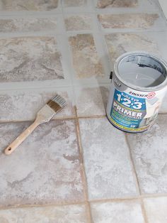 a paint can and brush sitting on the floor next to a tile pattern that looks like it has been grouted