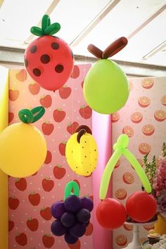 an assortment of fruits and vegetables hanging from the ceiling in front of a pink wall