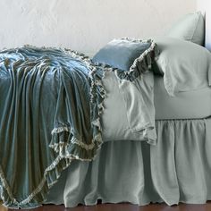 a bed with blue sheets and pillows on it's headboard, next to a white wall