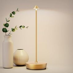 a white vase with a plant in it next to a gold lamp and a white vase