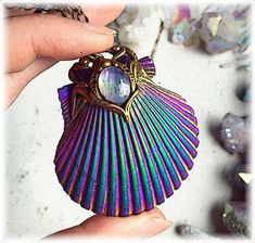 a hand holding a colorful shell shaped pendant