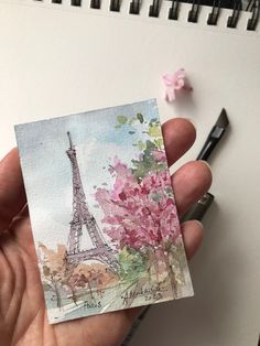 a person holding up a piece of paper with the eiffel tower in the background