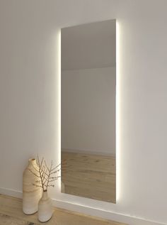 a white vase sitting next to a mirror on top of a wooden floor in front of a wall