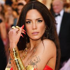 a woman in a red dress with gold jewelry on her arm and one hand up to her ear