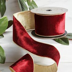 two rolls of red satin ribbon with gold trim on white table next to green leaves